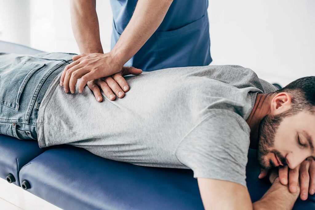 A chiropractor demonstrates a stretching exercise to a teenage athlete on a grassy sports field.
